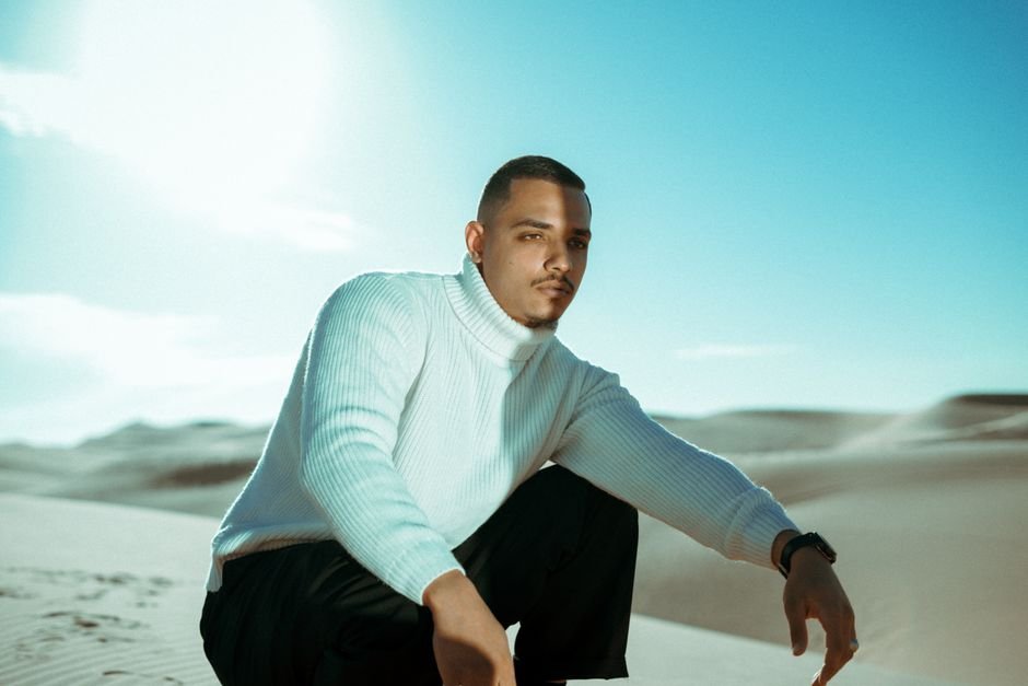 Portrait of a man in a white sweater crouching in a serene desert landscape.